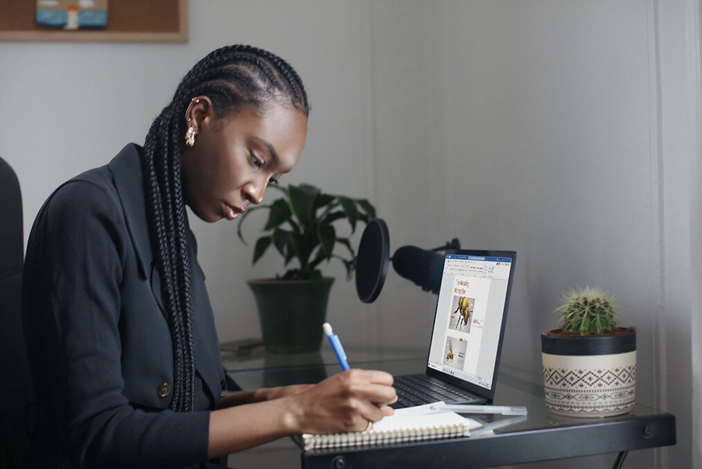 A person sitting in front of a computer while writing in a journal